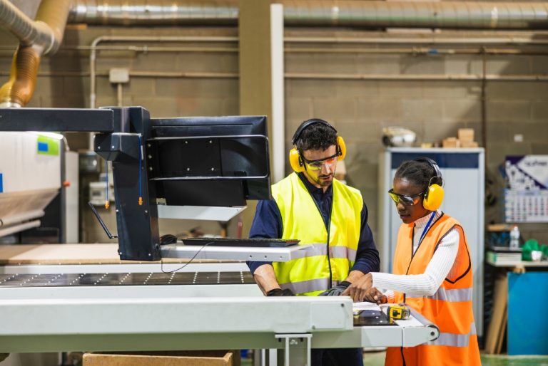 man and woman CNC setup operators looking at documents next to a CNC machine